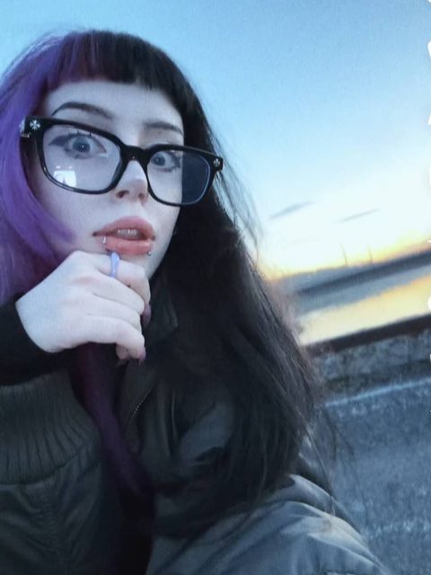 Two close-up outdoor selfies of a person with purple and black hair and glasses at dusk, one tilted at a sharp angle.
