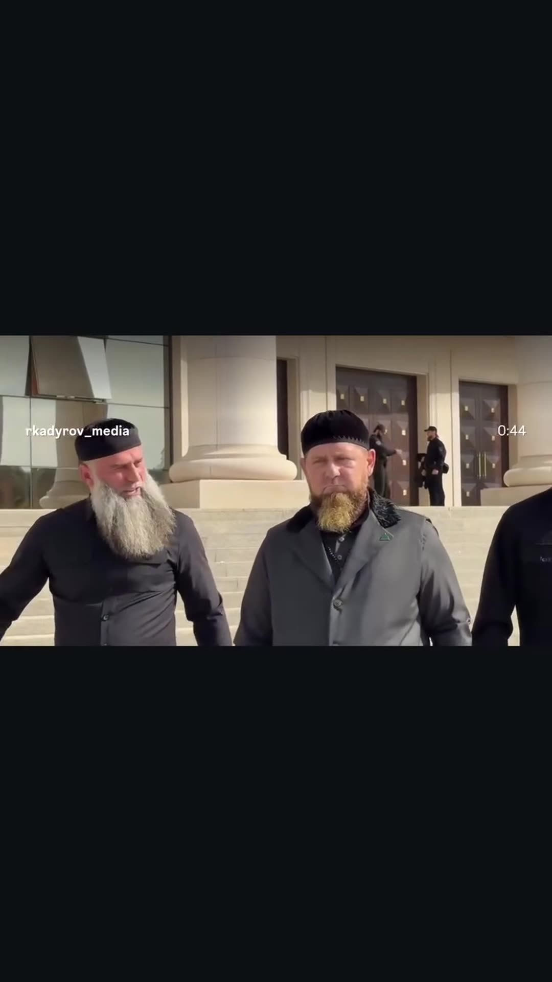 A story reshares a reel from @rkadyrov_media. A group of men in dark clothing and caps walks out of a large columned building and through a landscaped park. The clip then shows men standing inside a mosque and the group leaving the mosque, greeted by boys on the steps. The original caption says it…