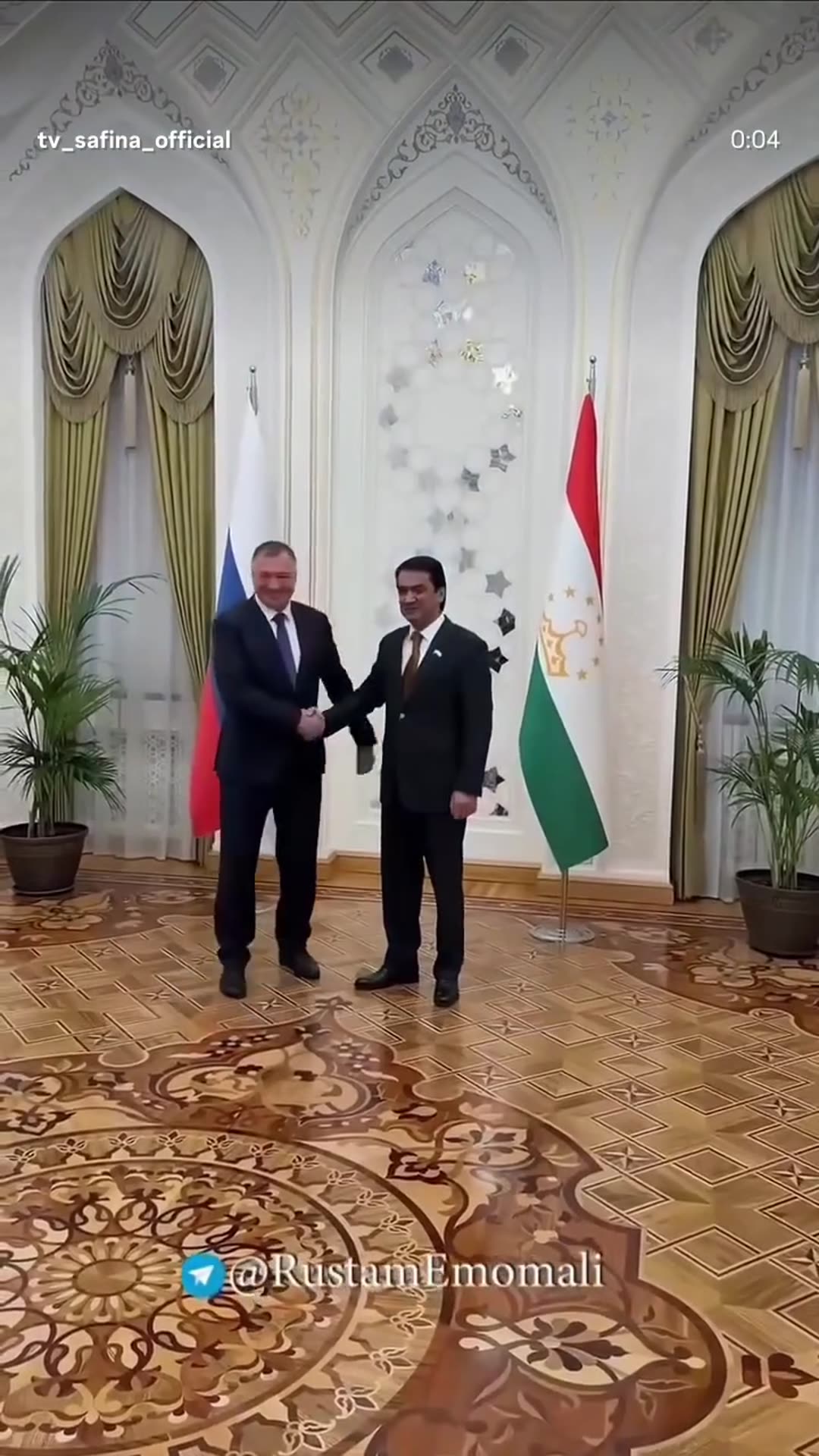 A story reshares a @tv_safina_official reel of a ceremonial greeting. A man in a dark suit stands between the Russian and Tajik flags in an ornate hall, a visitor walks in, and the two shake hands for the cameras.