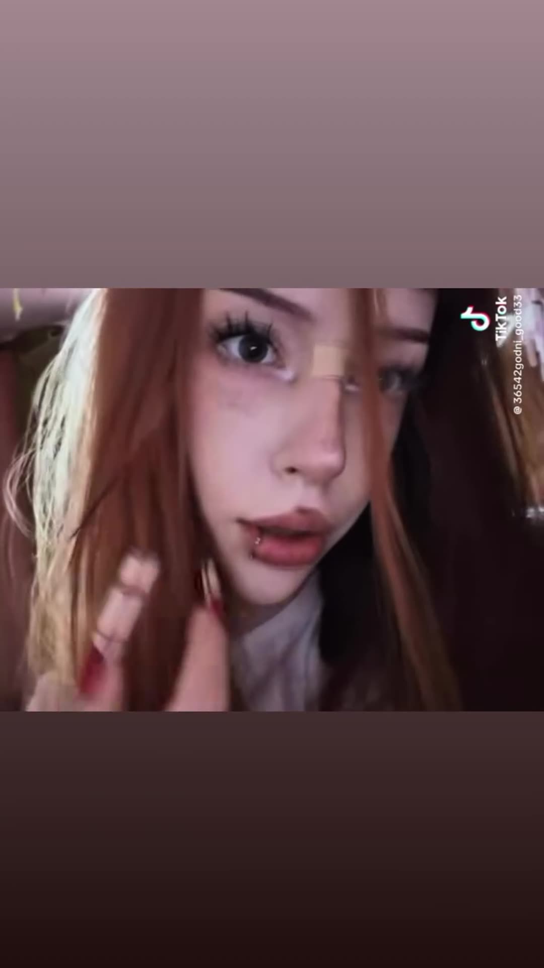 A story reposts a TikTok clip of a young woman with long red hair and a bandage on her nose, making playful faces close to the camera. The clip ends on a TikTok search-bar card showing the author's handle.