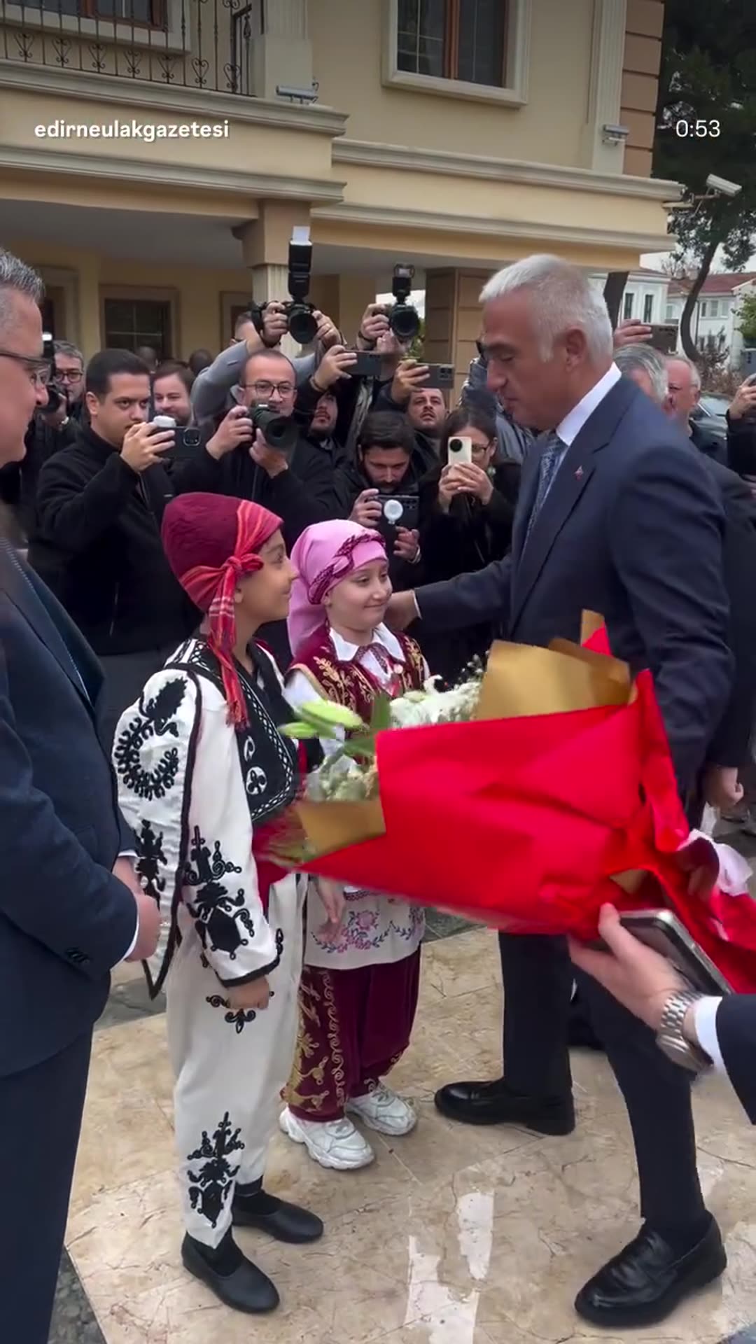 A story reshares a local news reel showing the Minister of Culture and Tourism being welcomed at the Edirne Governorship building, with folk-costumed children giving flowers, handshakes with officials, and the minister signing a book at a lectern, followed by a group photo.