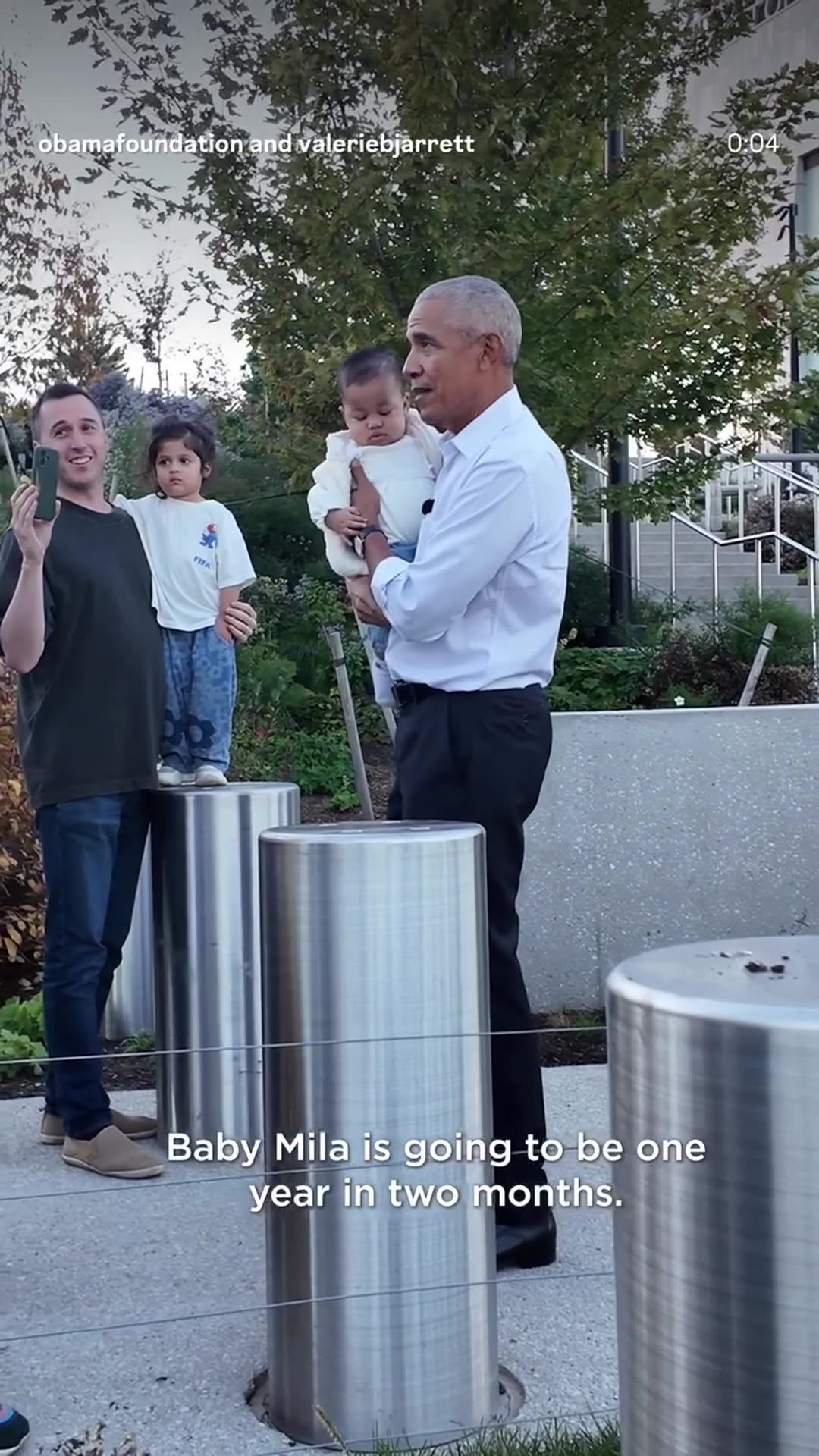 A story reshares the Obama Foundation's reel of a former president meeting a baby named Mila and her family and holding her at the Obama Presidential Center. He greets her warmly, asks her age and says she is a big girl while bystanders film.