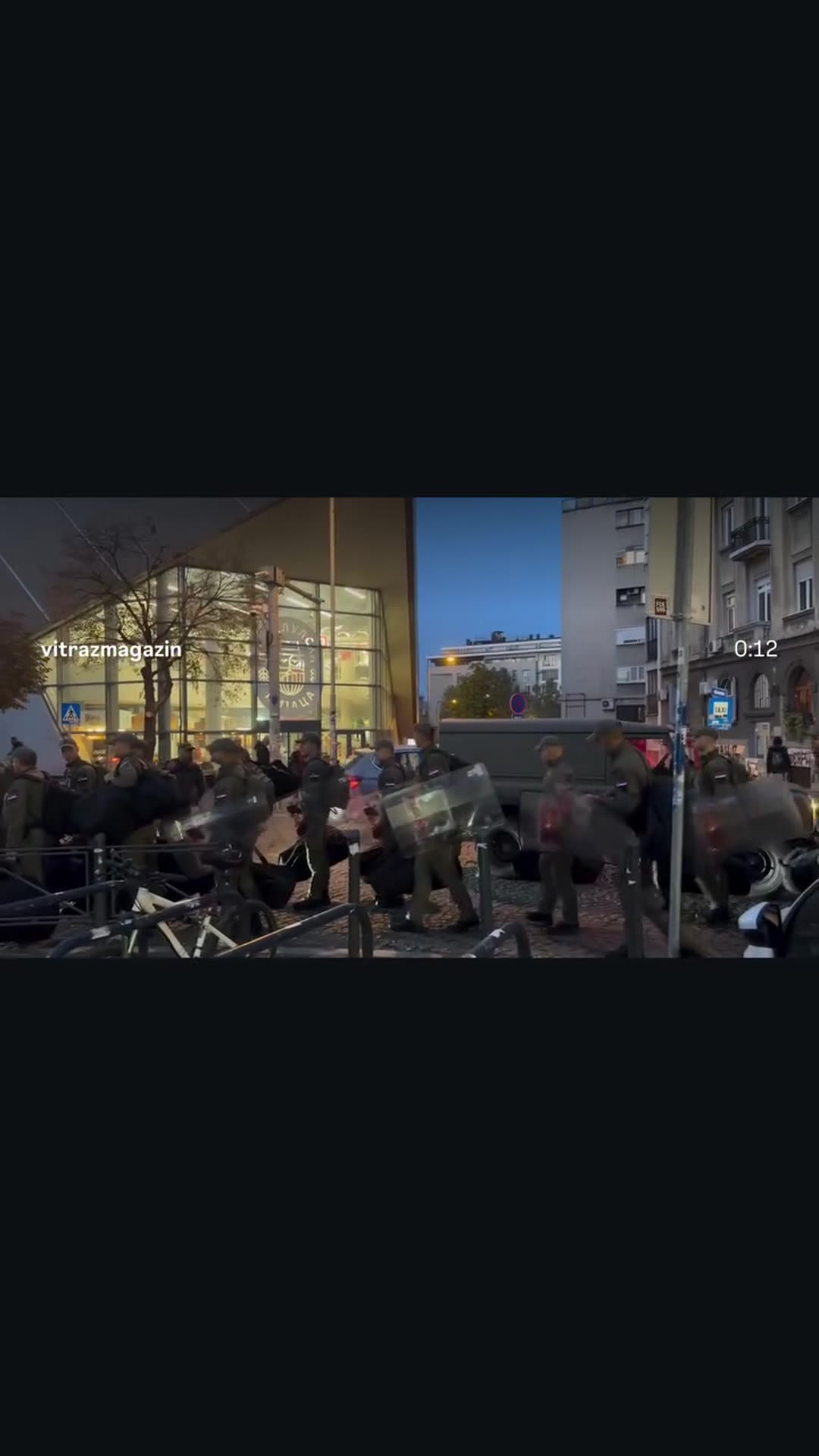 A story reshares Vitraž's reel showing a column of uniformed personnel with riot shields and bags walking past a military vehicle and a glass-fronted building in the evening. The original caption says the Gendarmerie is heading to RTS and calls it intimidation.