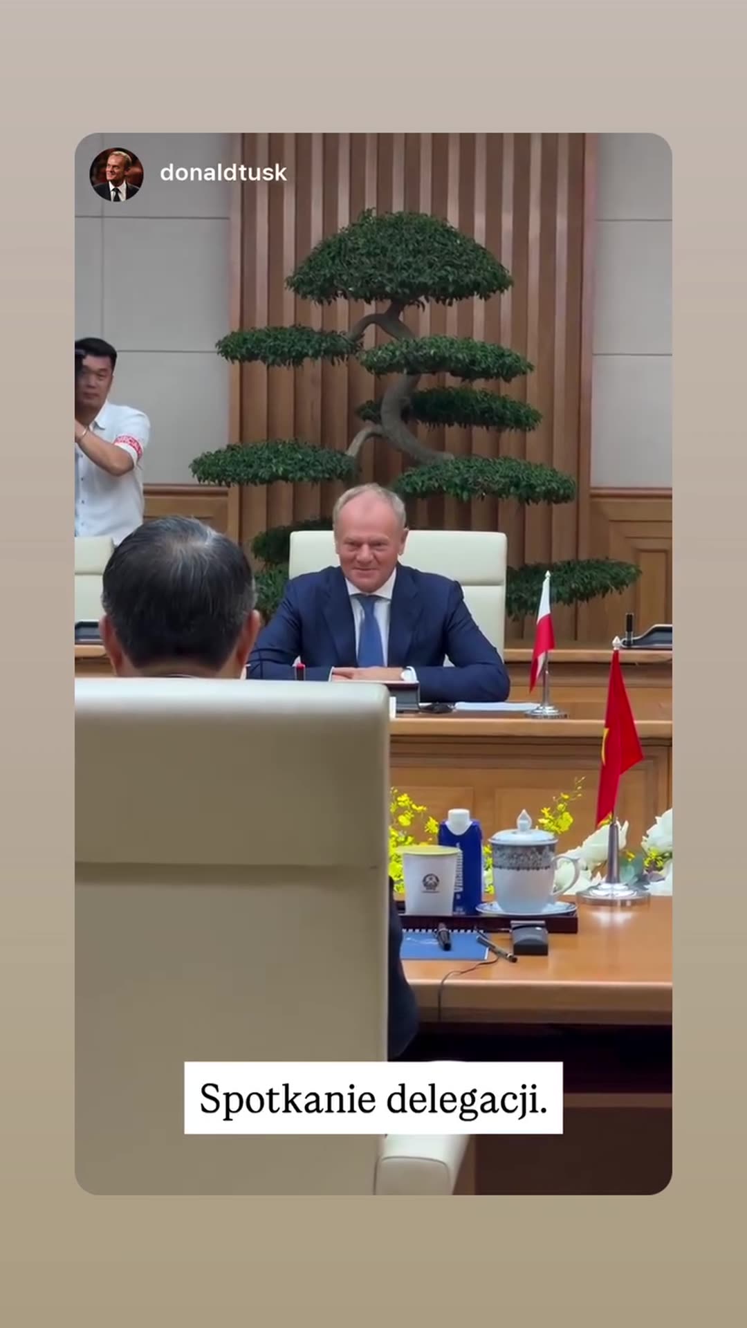 A story reshares a video from @donaldtusk's account showing a delegation meeting in a formal wood-panelled hall. It opens on a smiling Polish leader at the head of the table, then pans to the opposite delegation seated in rows. The Polish caption reads "Spotkanie delegacji" (delegation meeting).