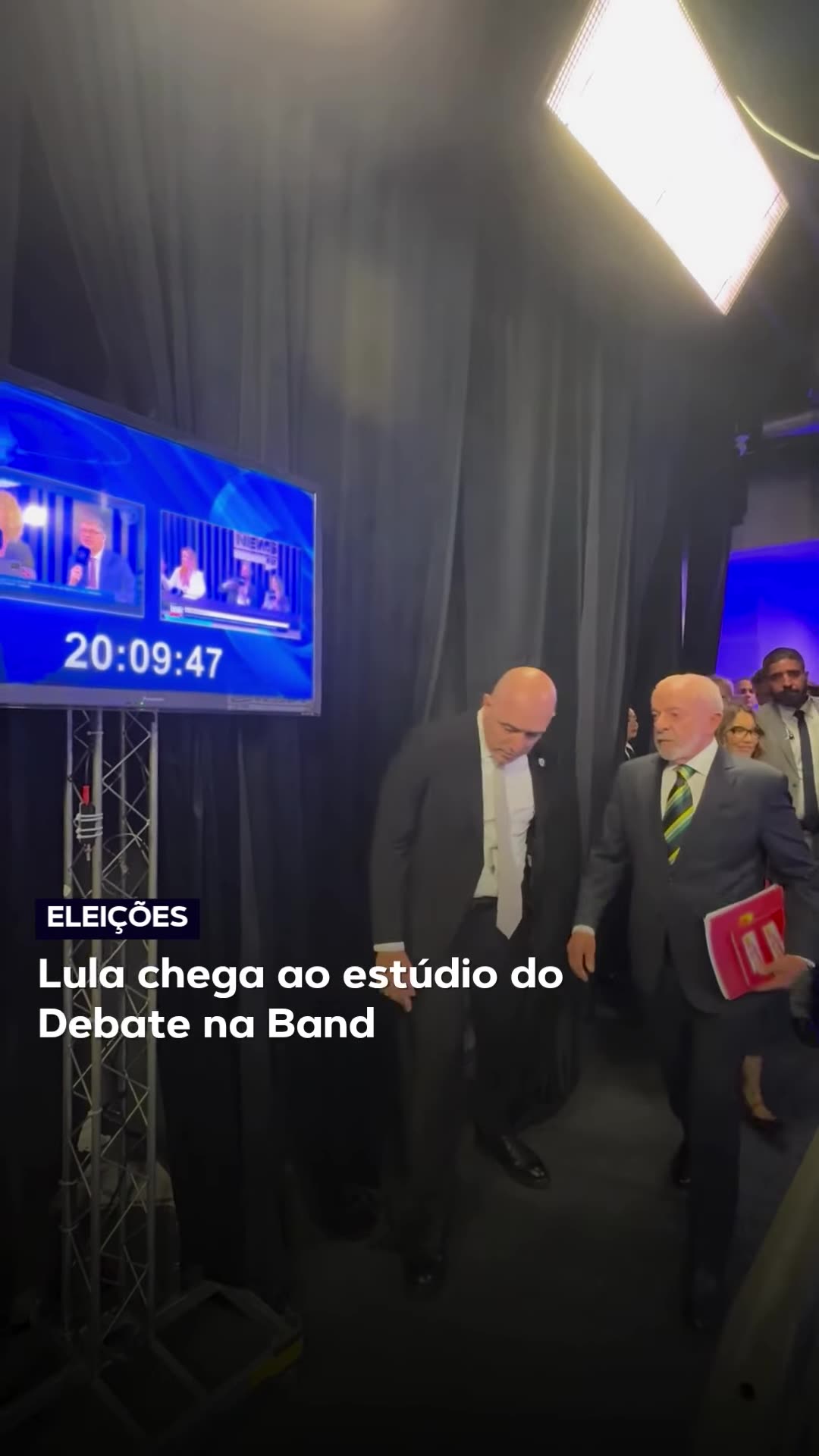 Backstage footage of Lula arriving at the Band studio for the presidential debate, surrounded by security, aides and press, with a reporter's narration.