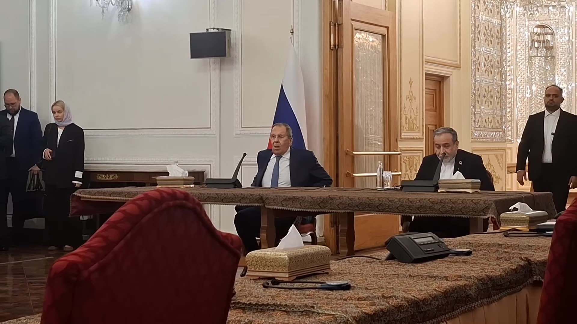 A reshared reel from the Iranian government information account shows the start of a joint press conference by the Iranian and Russian foreign ministers in an ornate hall. The two ministers enter, take their seats behind a table with microphones in front of the Russian flag, and staff stand nearby.