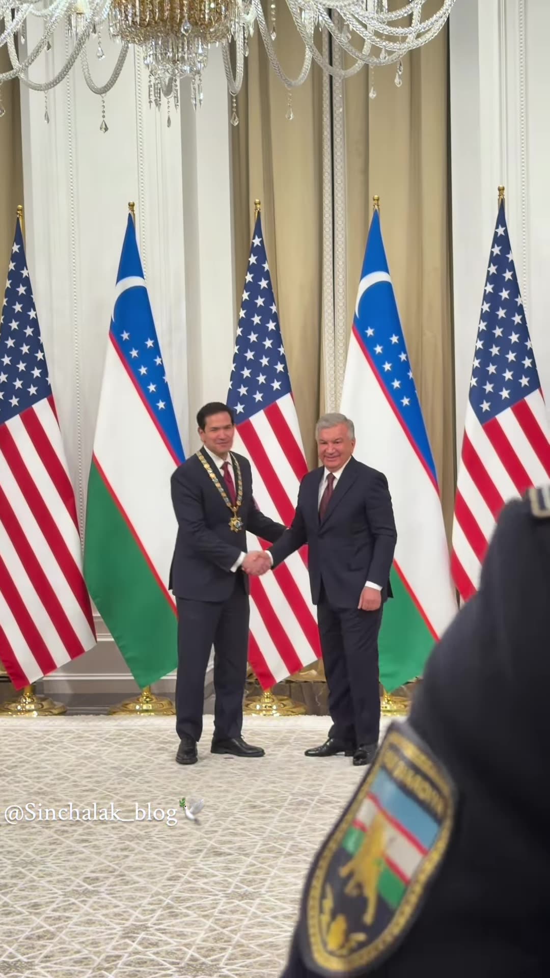 A reshared reel shows Uzbek President Shavkat Mirziyoyev awarding US Secretary of State Marco Rubio the order "For Great Services" in a hall hung with Uzbek and US flags. A guard carries in the award case and the collar is placed on Rubio's neck, followed by handshakes.