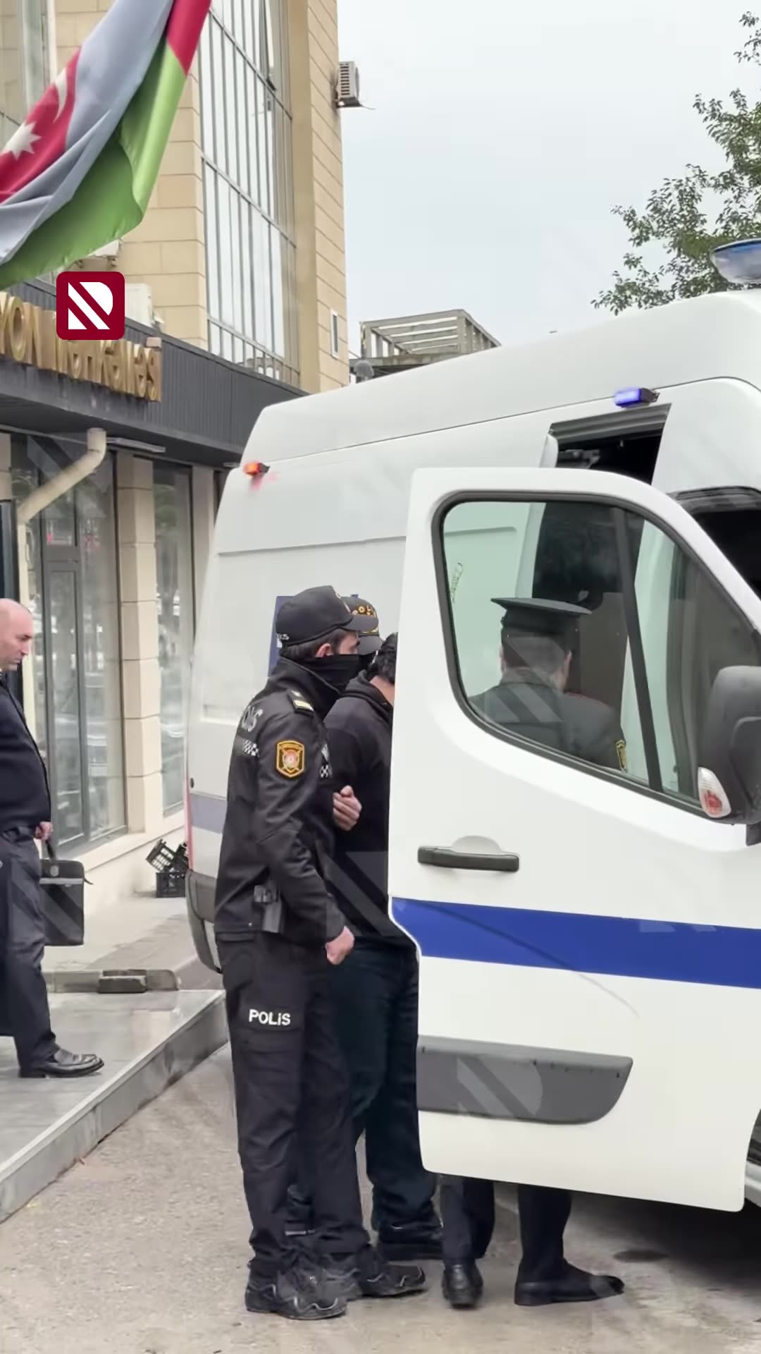 A repost of REAL TV's news reel showing police escorting people from the Baku court building to a police van, tied to the caption about a four-month detention order over a murder in a cafe.