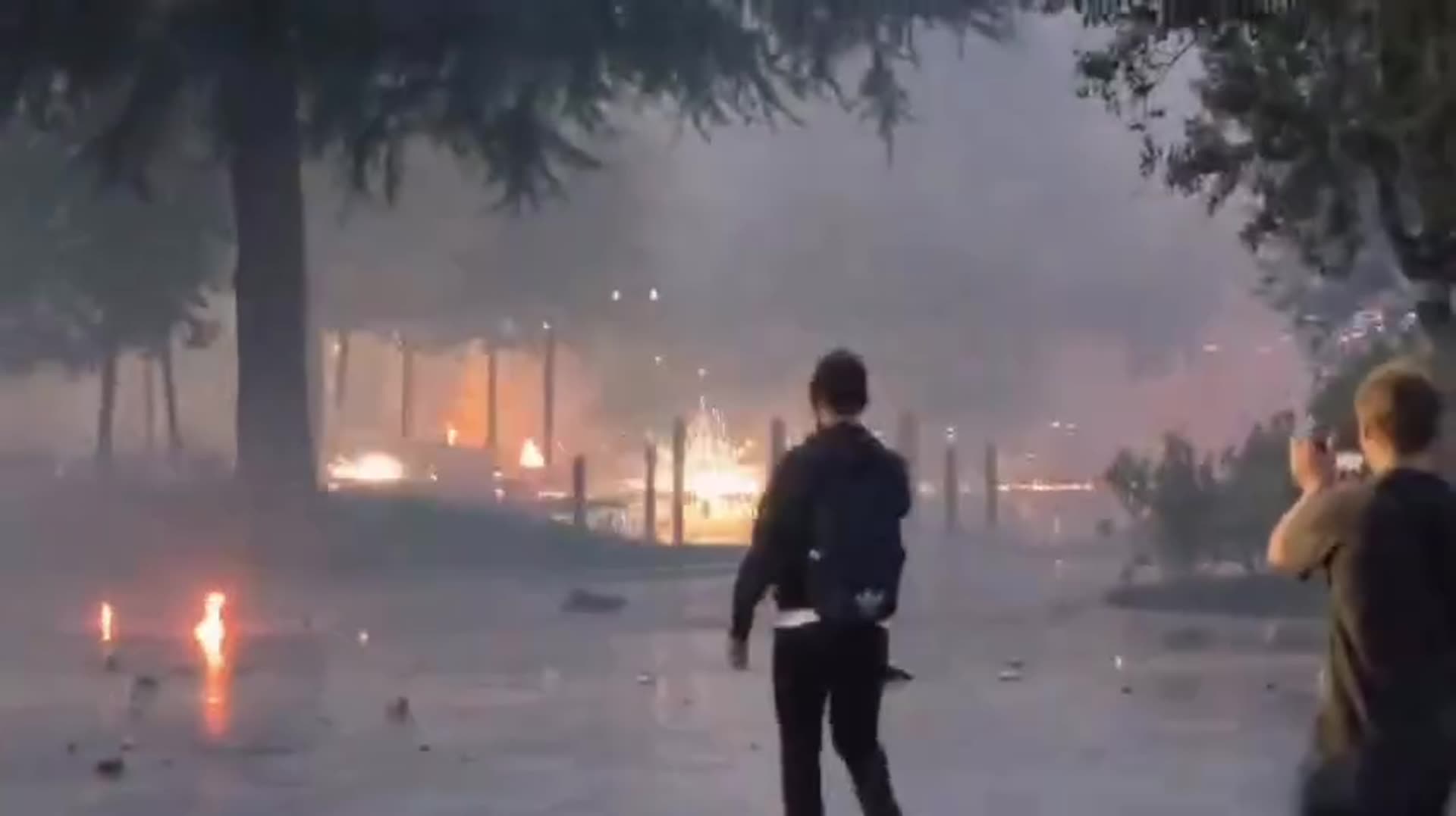 A repost of Edi Rama's reel showing footage of a violent protest at night: fires and fireworks or flares burning on a wet square, smoke drifting through trees, debris on the ground and bystanders filming. In the caption he condemns the violence and its instigators, and says he arranged hospital tre…