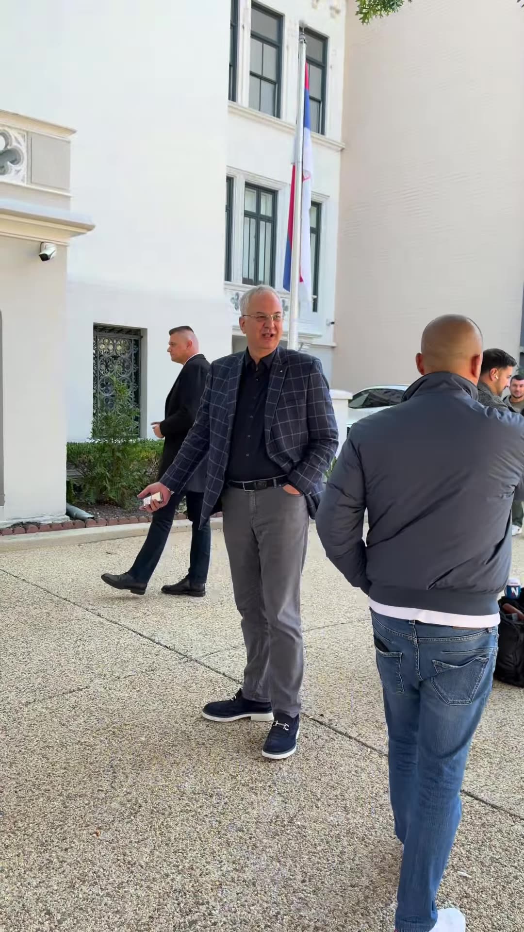 A reshared reel filmed outside the Embassy of the Republic of Serbia, probably in Washington. A group stands around a camera tripod and talks with a man in a checked blazer. Shouting about being "students" can be heard, apparently a heated exchange or protest. The man then walks into the embassy.